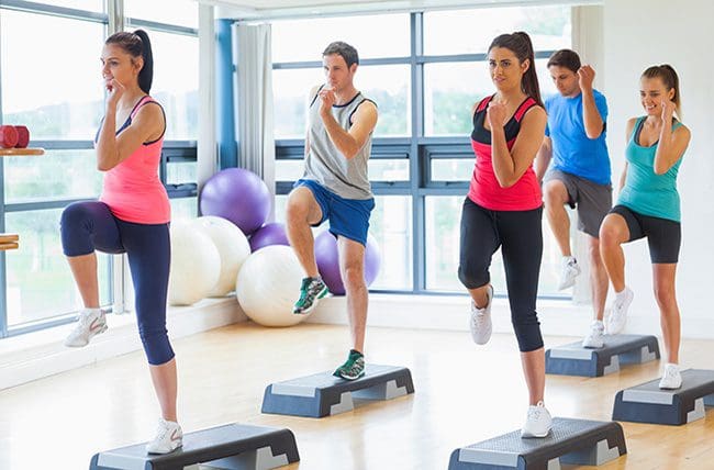 Instructor with fitness class performing step aerobics exercise